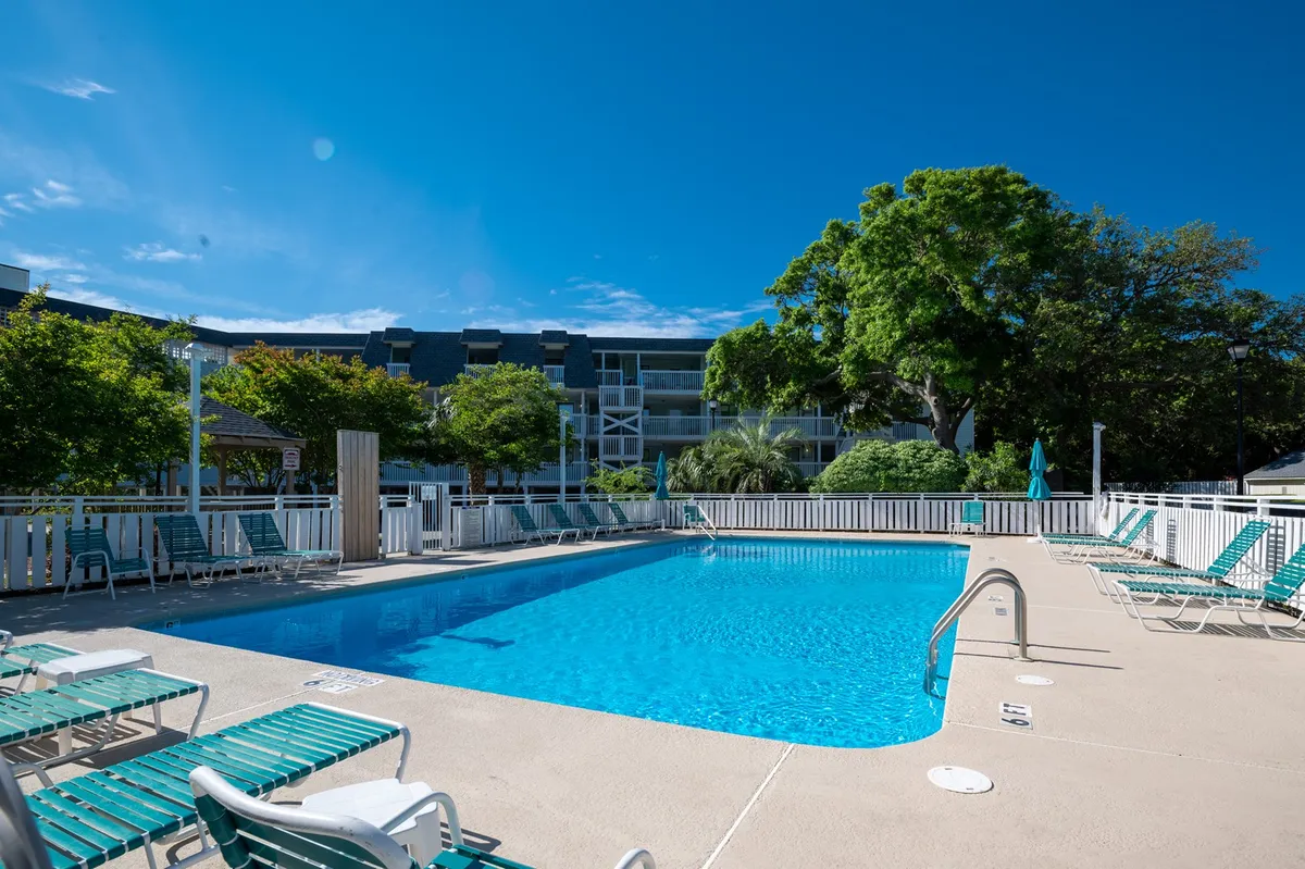 A sparkling swimming pool surrounded by lounge chairs, shady green trees, and a modern building in the background. The space invites both relaxation and social activity, suggesting options for swimming, sunbathing, or unwinding after excursions.
