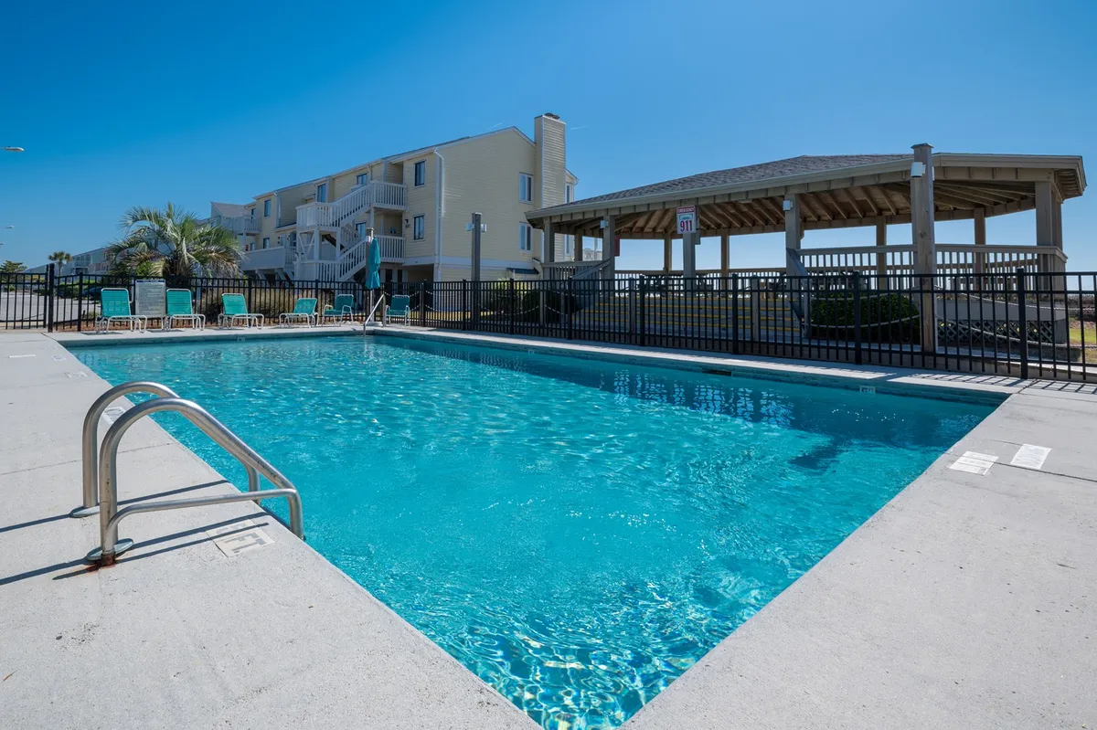 An inviting swimming pool bordered by lounge chairs and a charming gazebo. The area is designed for relaxation, sunbathing, and poolside social gatherings under the coastal sky.