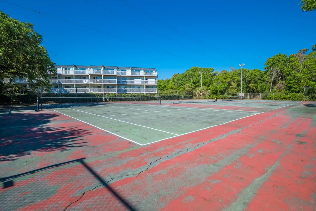 The exterior tennis court is bordered by lush greenery, with lines and nets ready for play. Nearby balconies hint at the resort environment, and the scene is set for friendly matches and outdoor activity.