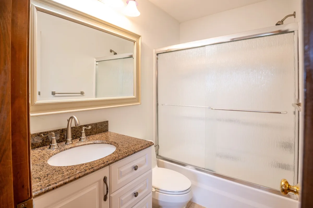A stylish bathroom with a granite countertop, large mirror, and modern shower area. The thoughtful design ensures a refreshing, spa-like experience, suitable for personal grooming and relaxation. The space is spotlessly clean, alluding to the fresh linens and high standards of hospitality described.