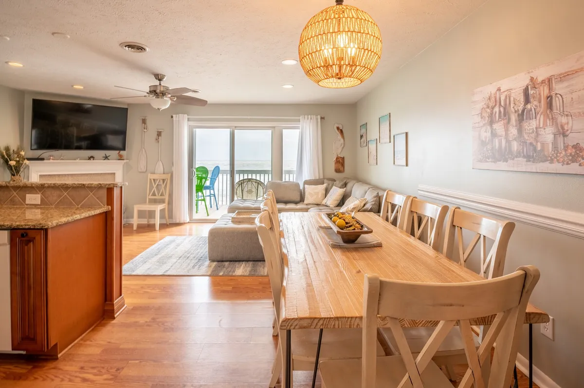 A cozy yet spacious scene featuring a large sectional sofa and a natural wood dining table beneath a decorative pendant light. The setup encourages both relaxation and group gatherings, perfectly blending comfort and sociability.