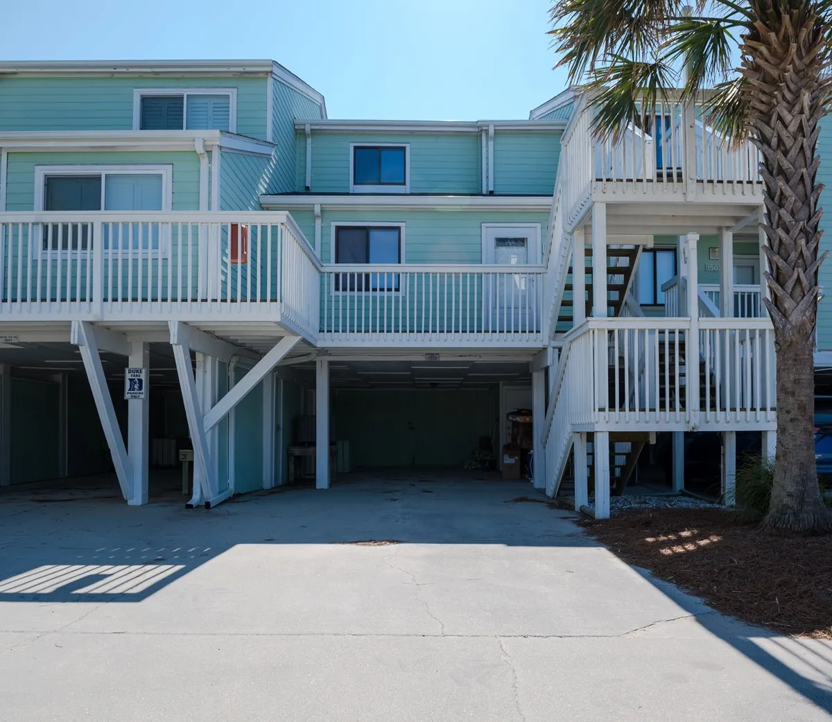 This image shows the home's exterior with a palm tree, stairway, balcony, and windows—providing a sense of the oceanfront location and the inviting entryway to the property. The balcony hints at spaces where guests can relax and enjoy the ocean air, reinforcing the promise of alfresco dining and ocean breezes.